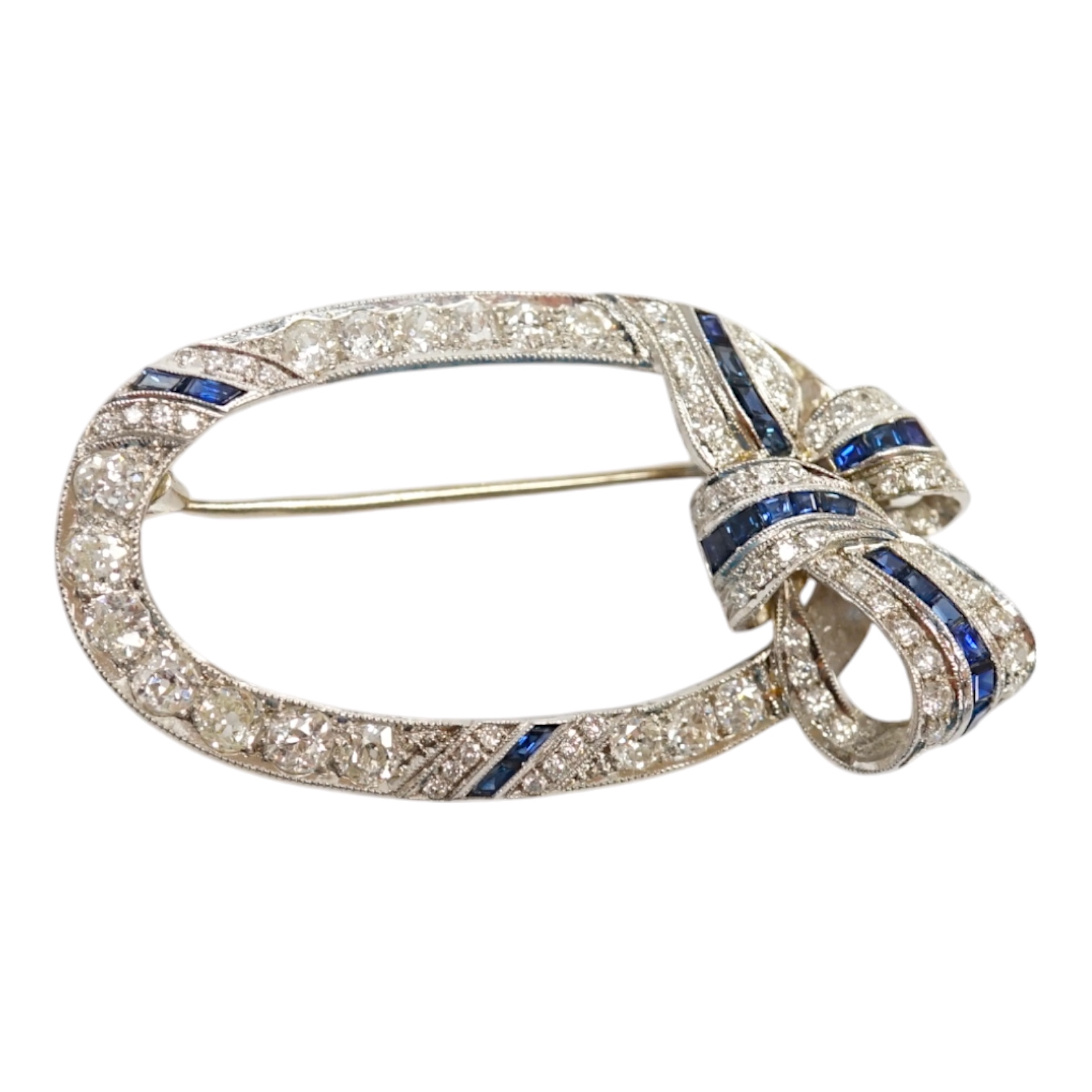 A yellow and white metal, sapphire and millegrain set diamond cluster oval open work brooch, with ribbon bow motif, 50mm, gross weight 11 grams. Condition - good